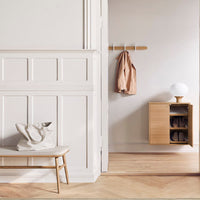 Light wood bench and cabinet against a soft beige and white wall, with a neutral-toned coat and bag for a modern, minimalist look.