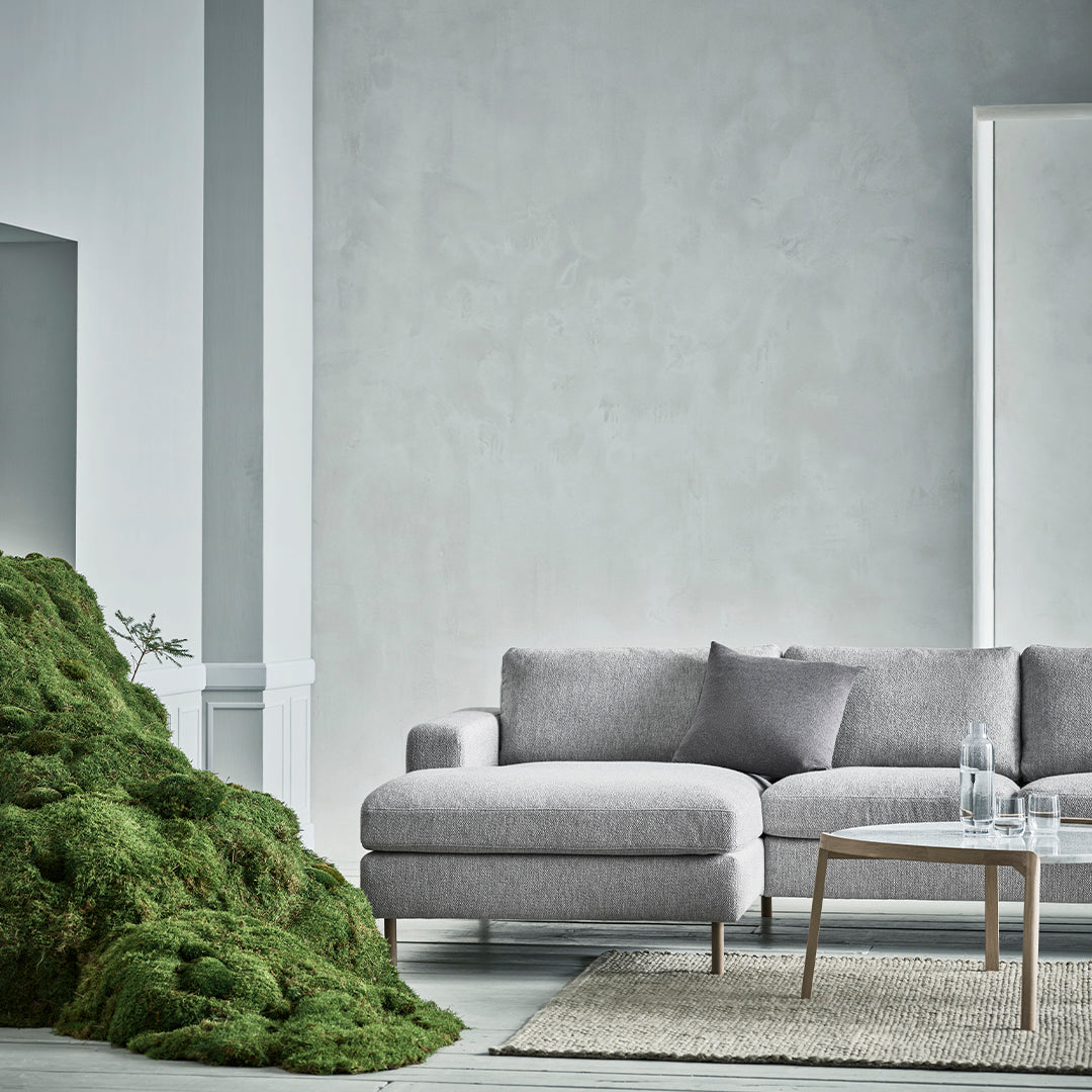 Gray sectional sofa with a soft texture, complemented by a green moss arrangement and neutral-toned rug.