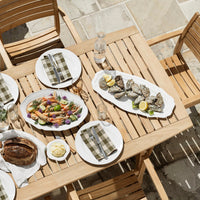 "Outdoor dining table with green and white checkered napkins, colorful food platters, and natural wood tones."