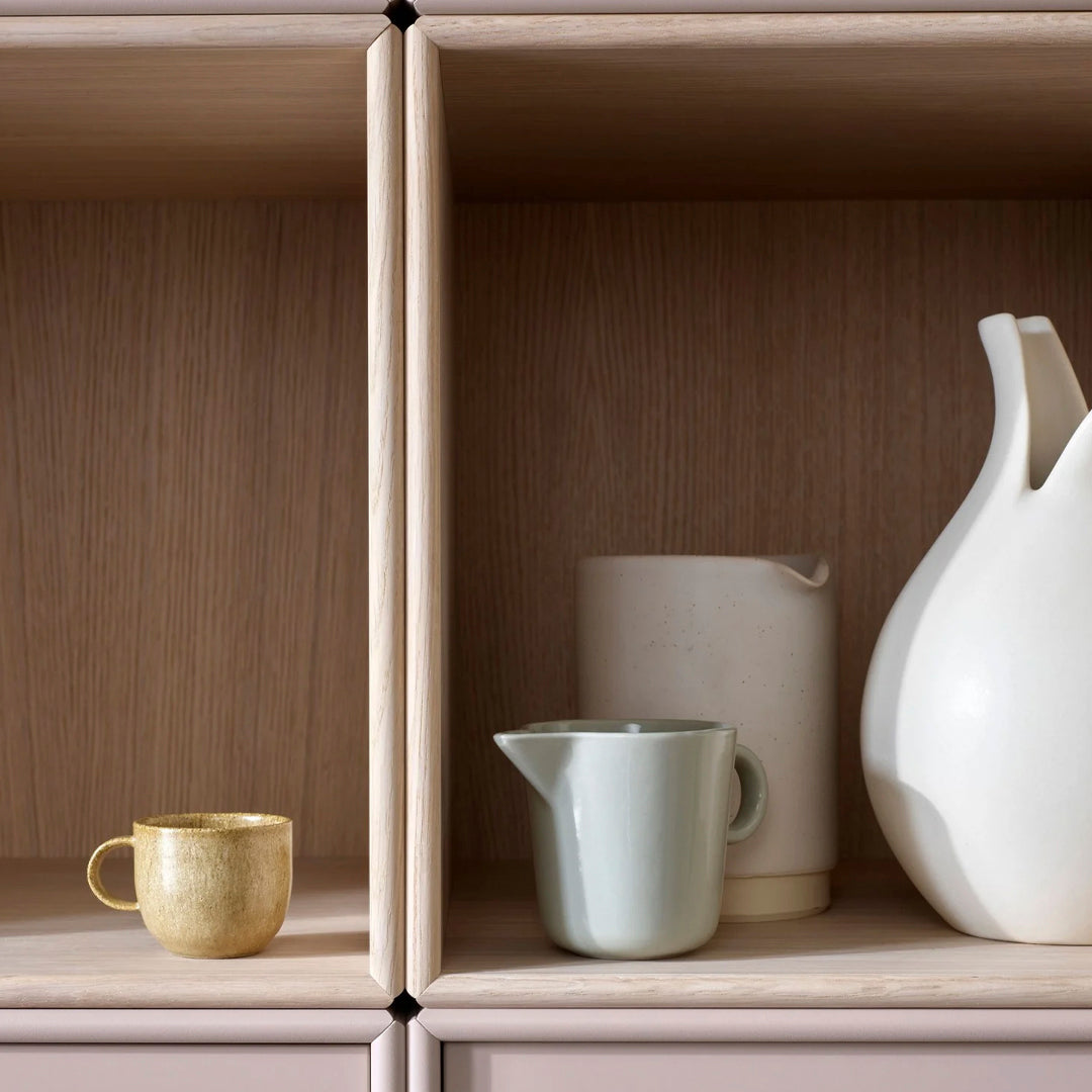 Decorative kitchenware in gold, mint green, beige, and white, displayed on natural wood shelves. Stylish and modern design.
