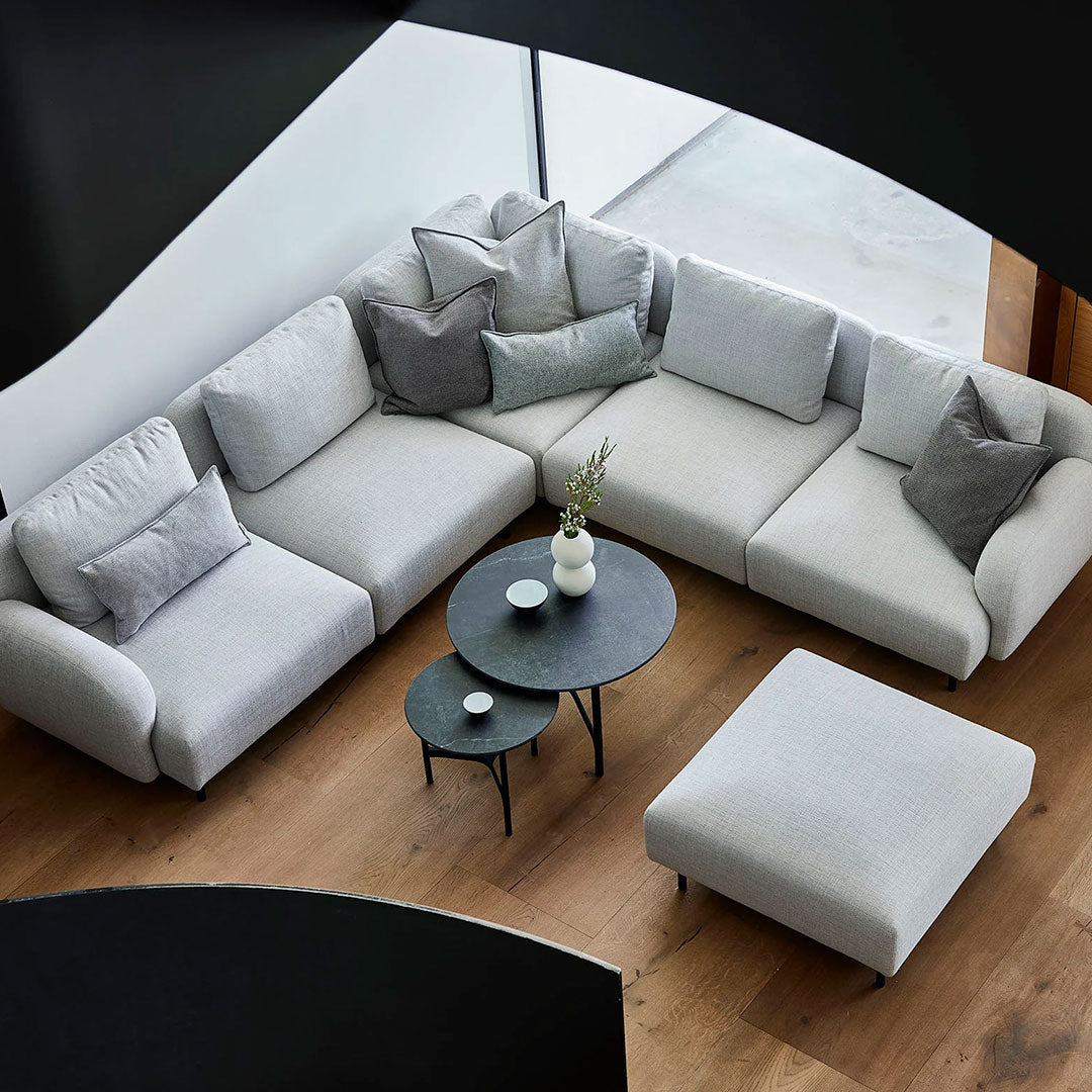 Light gray sectional sofa with dark gray accent pillows, circular black coffee table, and wooden floor. Modern design.