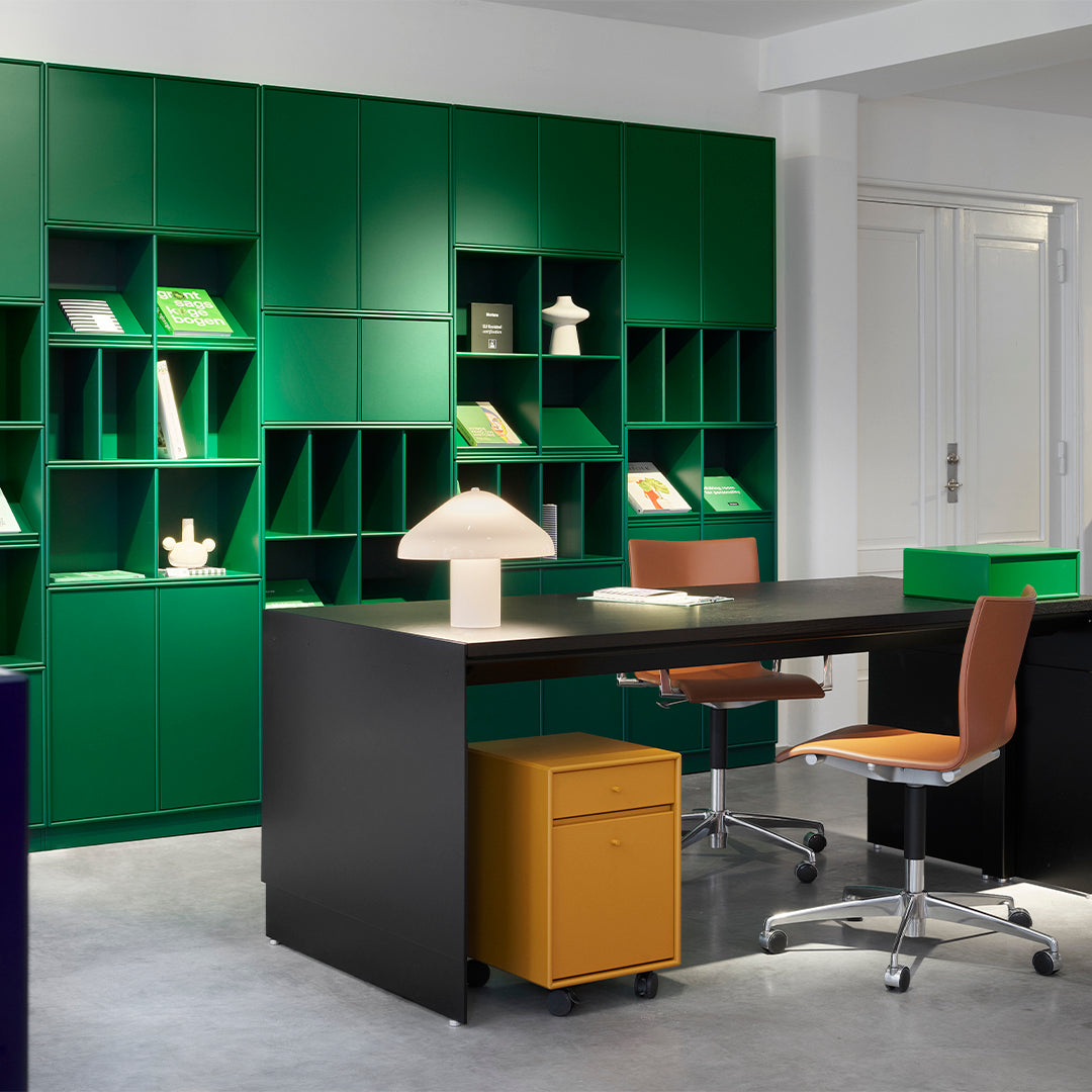 Modern workspace featuring vibrant green shelves, warm orange chairs, and a sleek black desk with a yellow storage unit.
