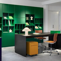 Modern workspace featuring vibrant green shelves, warm orange chairs, and a sleek black desk with a yellow storage unit.