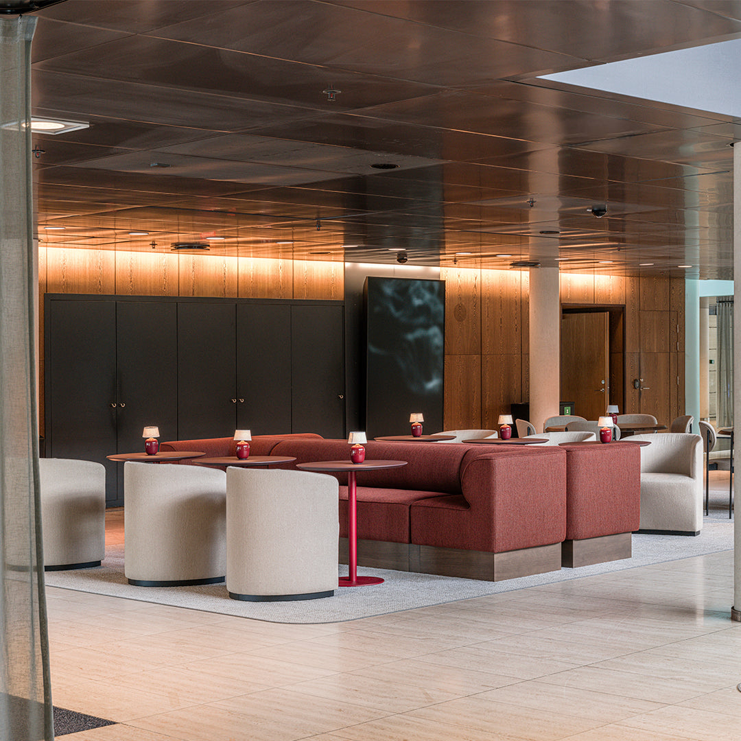 Modern lounge with red and beige seating, sleek wood accents, and a polished metallic ceiling.