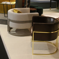 Curved chairs in cream and dark brown leather with sleek gold accents on a modern white backdrop.