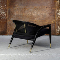 Black and gold accent chair featuring a sleek woven back and minimalist design against a textured industrial backdrop.