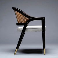 Elegant black chair with rattan backrest, upholstered in soft gray fabric, featuring gold accents on legs.