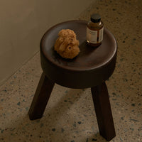 Brown wooden stool with a smooth round seat and dark legs, featuring a natural texture. Perfect for modern decor.