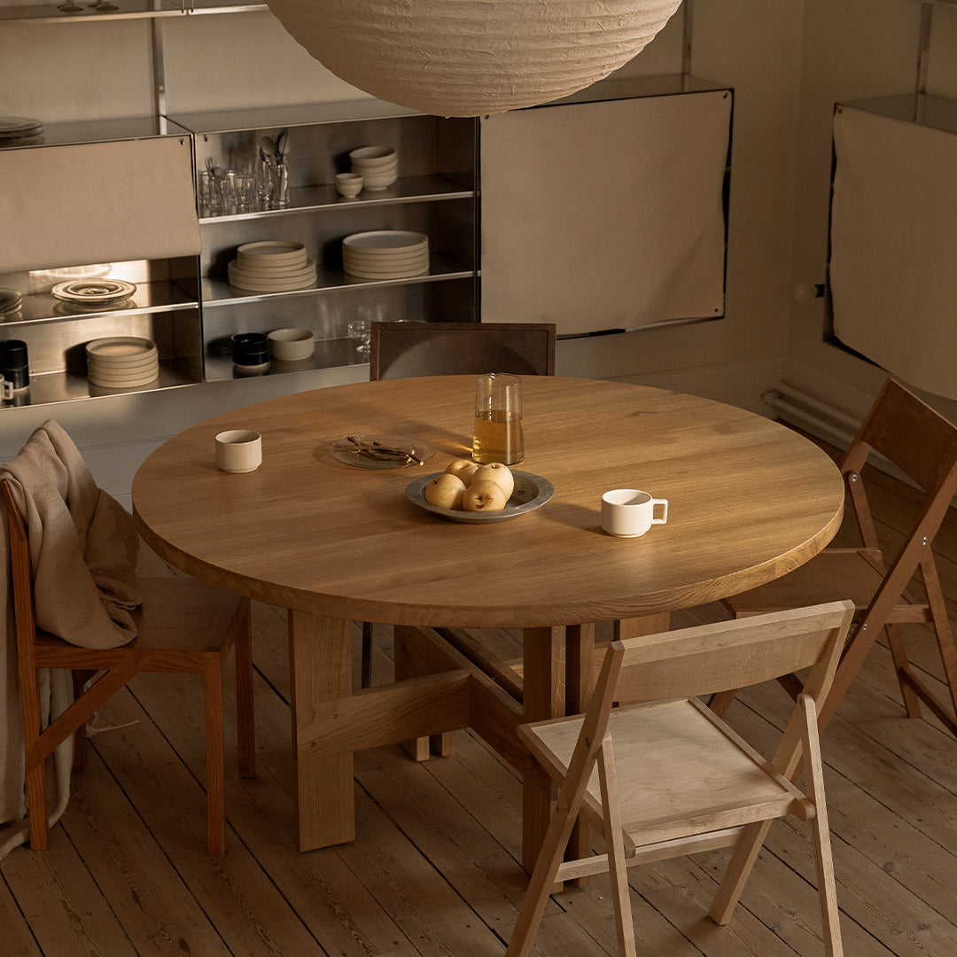 Natural wood round dining table with warm tones, paired with light beige and soft cream accents in a cozy setting.