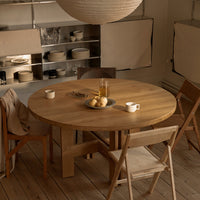 Natural wood round dining table with warm tones, paired with light beige and soft cream accents in a cozy setting.