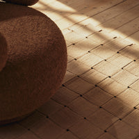Brown textured round pouf on a patterned wooden floor with subtle light and shadow play.