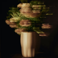 Blurred bouquet of soft pink flowers in a sleek white vase against a dark background. Elegant and artistic design.