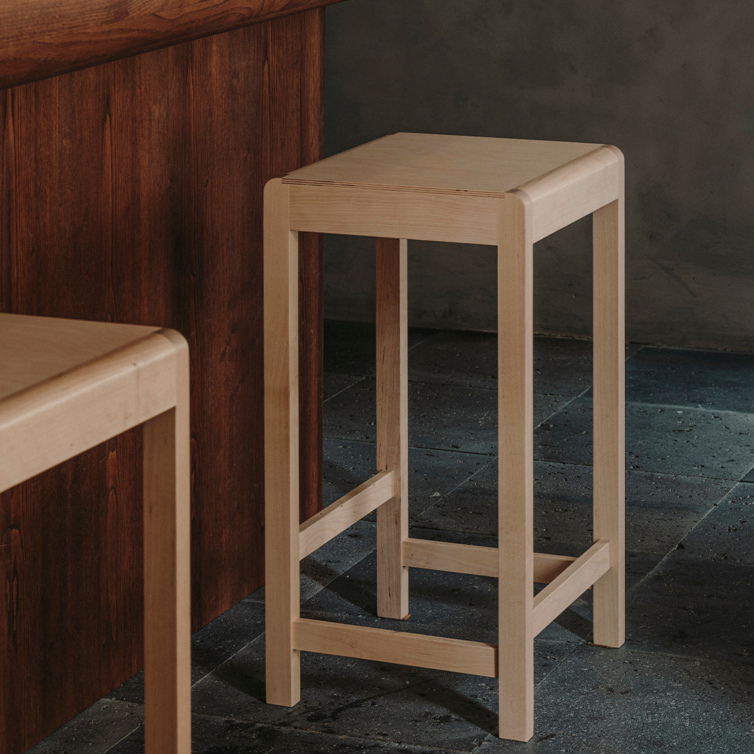Beige wooden bar stool with a minimalist design, featuring clean lines and a smooth, simple finish.