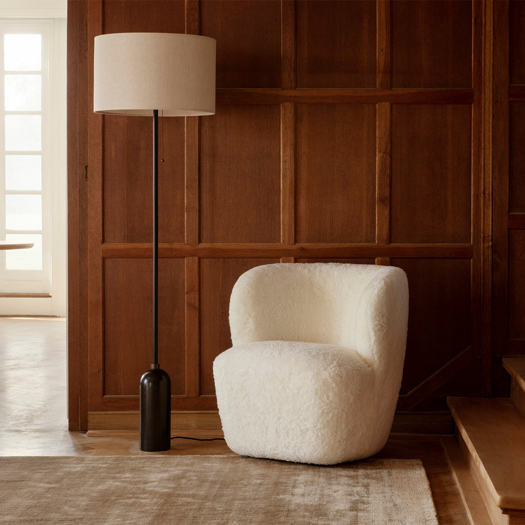 Cream-colored boucle chair with soft, rounded edges, paired with a sleek black floor lamp against wooden paneling.