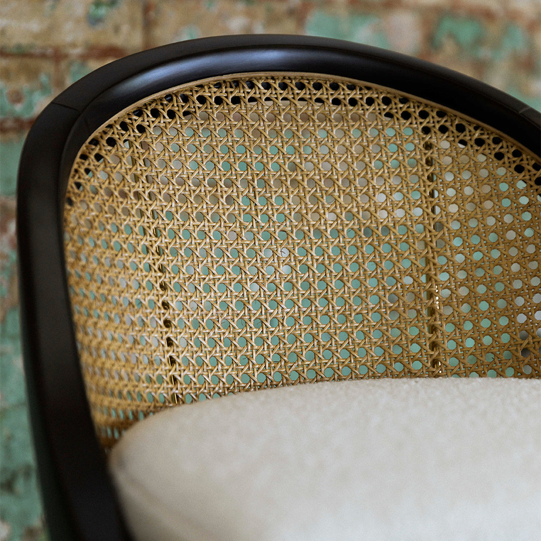 Rattan chair detail featuring woven natural fibers and a sleek black frame against a textured green backdrop.
