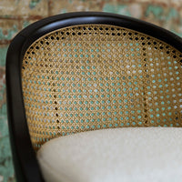 Black and gold woven chair detail with a cream cushion on a textured, colorful background.