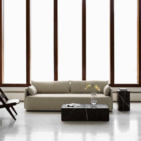 Minimalist beige sofa with a black marble coffee table, set against bright, modern windows. Elegant neutral palette.