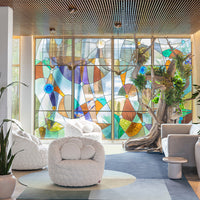 "Vibrant stained glass window with geometric patterns in blue, green, amber, and clear hues, adding color to the modern space."