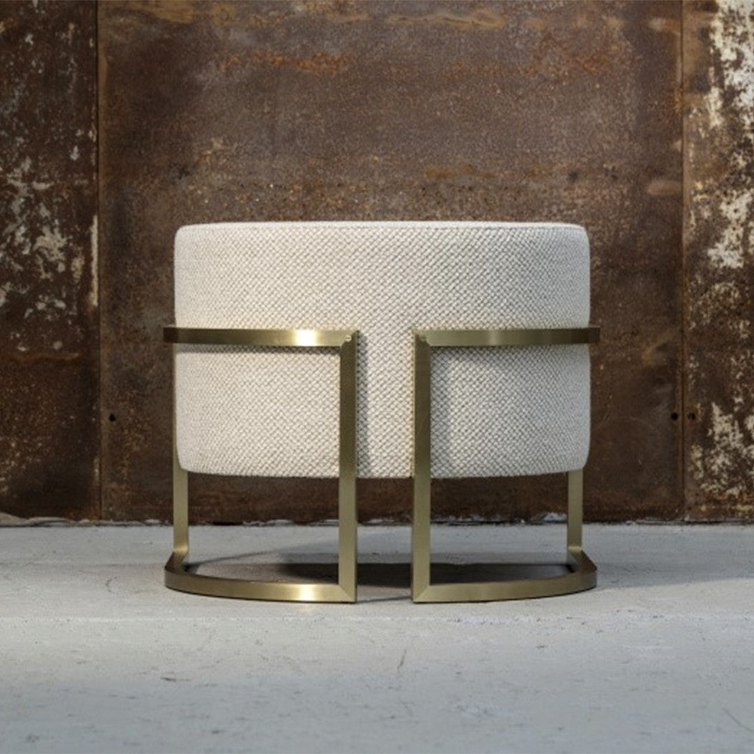 Round cream ottoman with textured fabric and modern brass frame, adding a stylish touch to any decor.