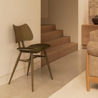 Olive green mid-century modern chair against a minimalist backdrop with wooden elements and soft beige tones.