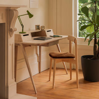 Light wood desk with minimalist design; soft brown chair and green lamp add a pop of color against the neutral backdrop.