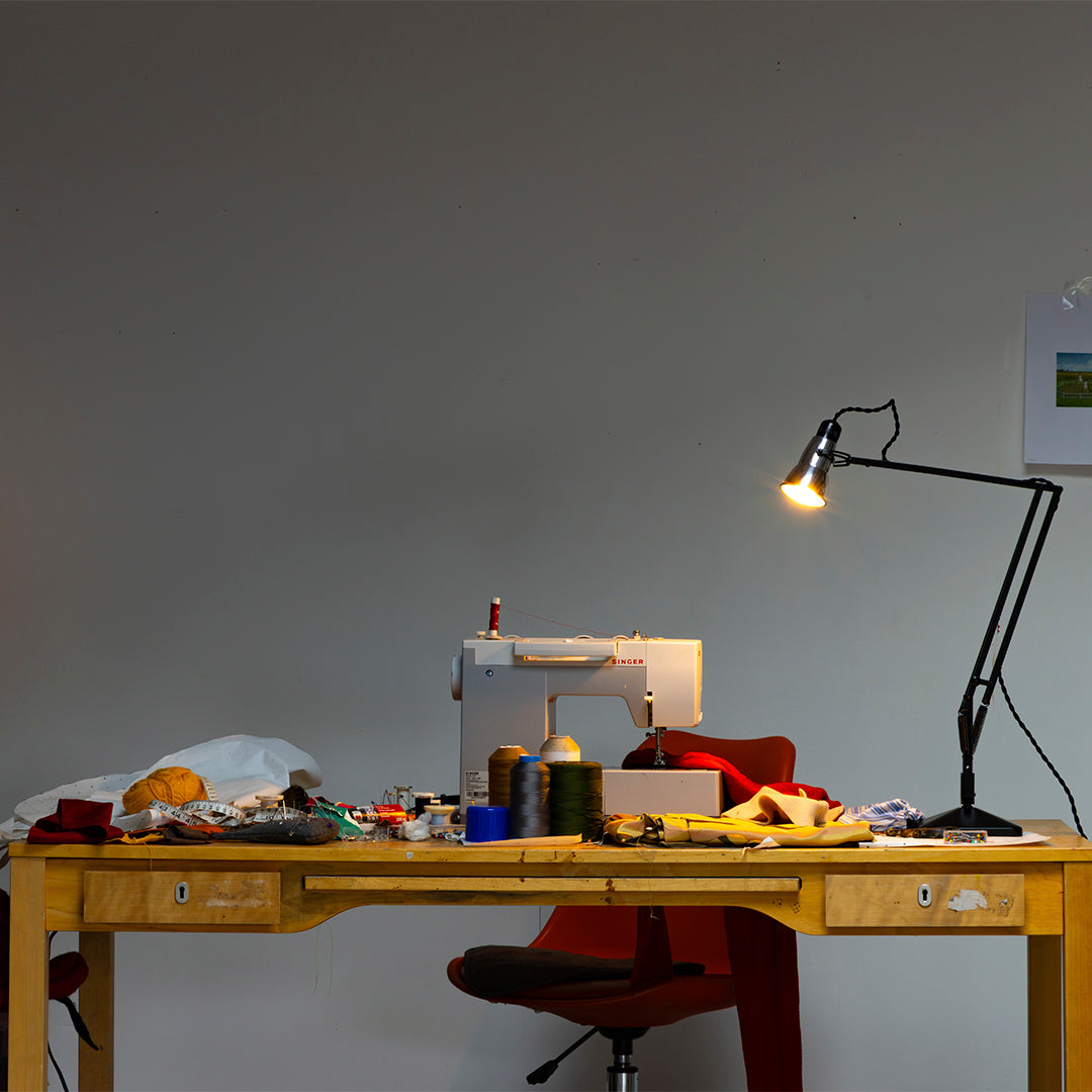 Sewing workspace featuring colorful threads, fabrics, and a modern lamp against a neutral wall backdrop.