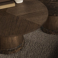 Brown round coffee table with textured wood grain pattern and dark circular base, set on a light, plush carpet.