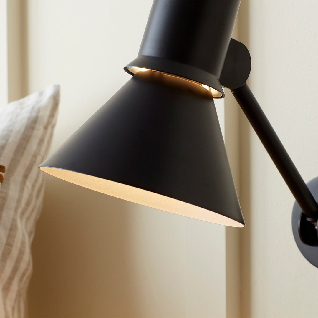 Black cone lampshade with gold interior, minimalist design against a light-colored wall. Perfect for modern decor.