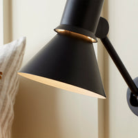 Black cone lampshade with gold interior, minimalist design against a light-colored wall. Perfect for modern decor.