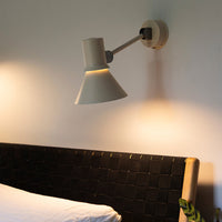 Modern wall lamp with a soft beige shade and contrasting black mounting, illuminating a stylish, dark woven bed frame.