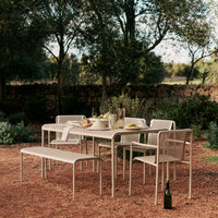 Light beige outdoor dining set featuring a perforated pattern, surrounded by lush greenery and rustic stone walls.