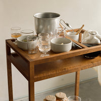 Wooden serving cart featuring warm brown tones, clear glassware, and soft cream dinnerware. Inviting and elegant presentation.
