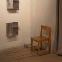 Light wood chair against a neutral wall, with silver metal shelves adding modern contrast. Warm tones create inviting ambiance.