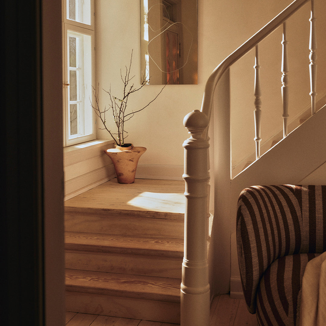 Warm beige tones with striped brown and cream fabric on the couch, accented by natural light and a minimalist vase.