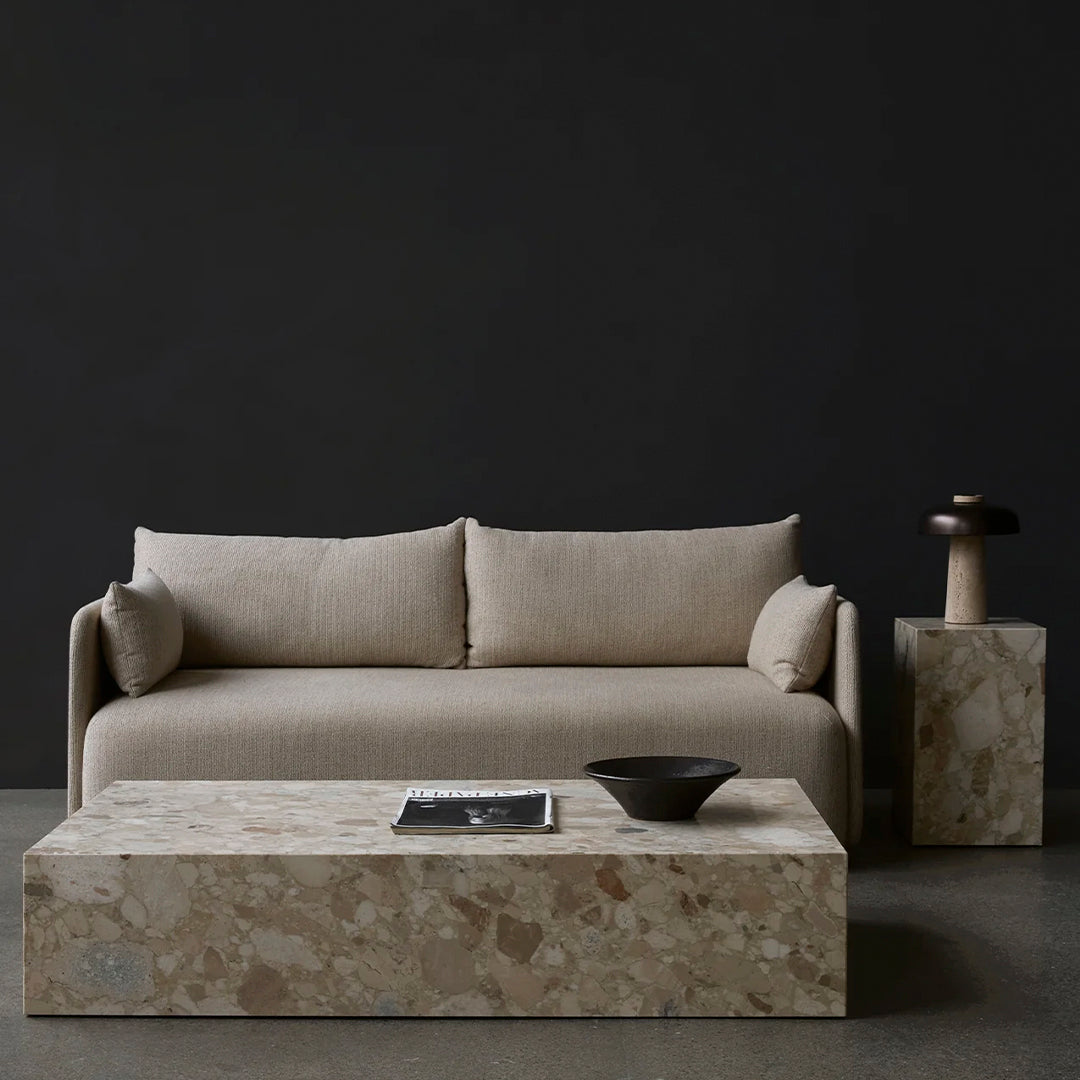 Beige sofa with plush cushions, paired with a textured stone coffee table and dark background for contrast.