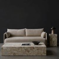 Beige sofa with plush cushions, paired with a textured stone coffee table and dark background for contrast.