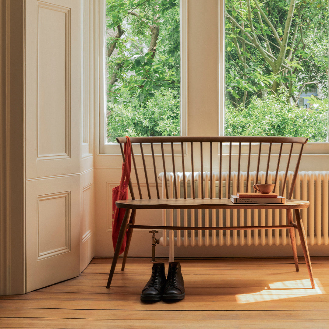 "Natural wood bench with a sleek design, featuring dark brown slats and a red accent cushion against a bright backdrop."
