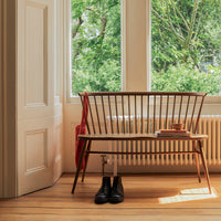 "Natural wood bench with a sleek design, featuring dark brown slats and a red accent cushion against a bright backdrop."