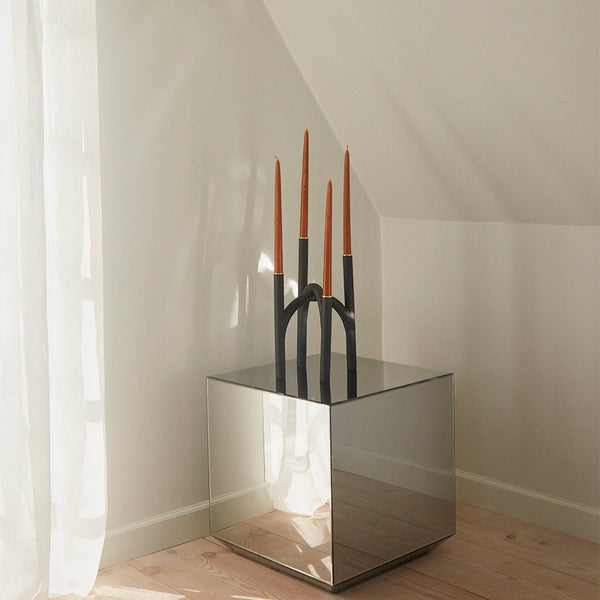 "Black candle holder with copper-tipped candles on a mirrored table, accented by soft natural lighting."