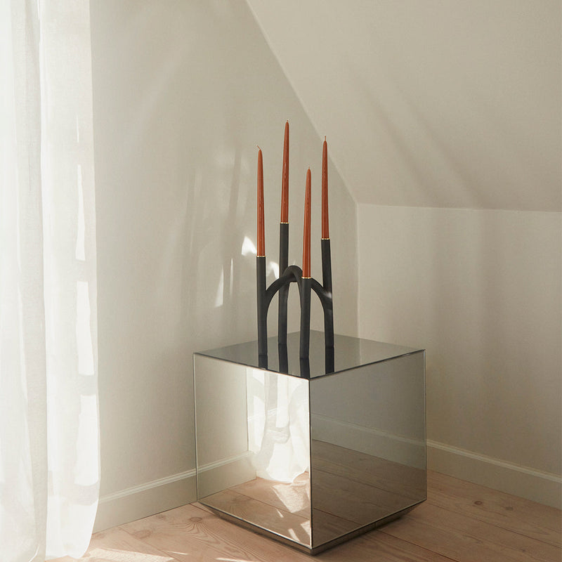 "Black candle holder with copper-tipped candles on a mirrored table, accented by soft natural lighting."
