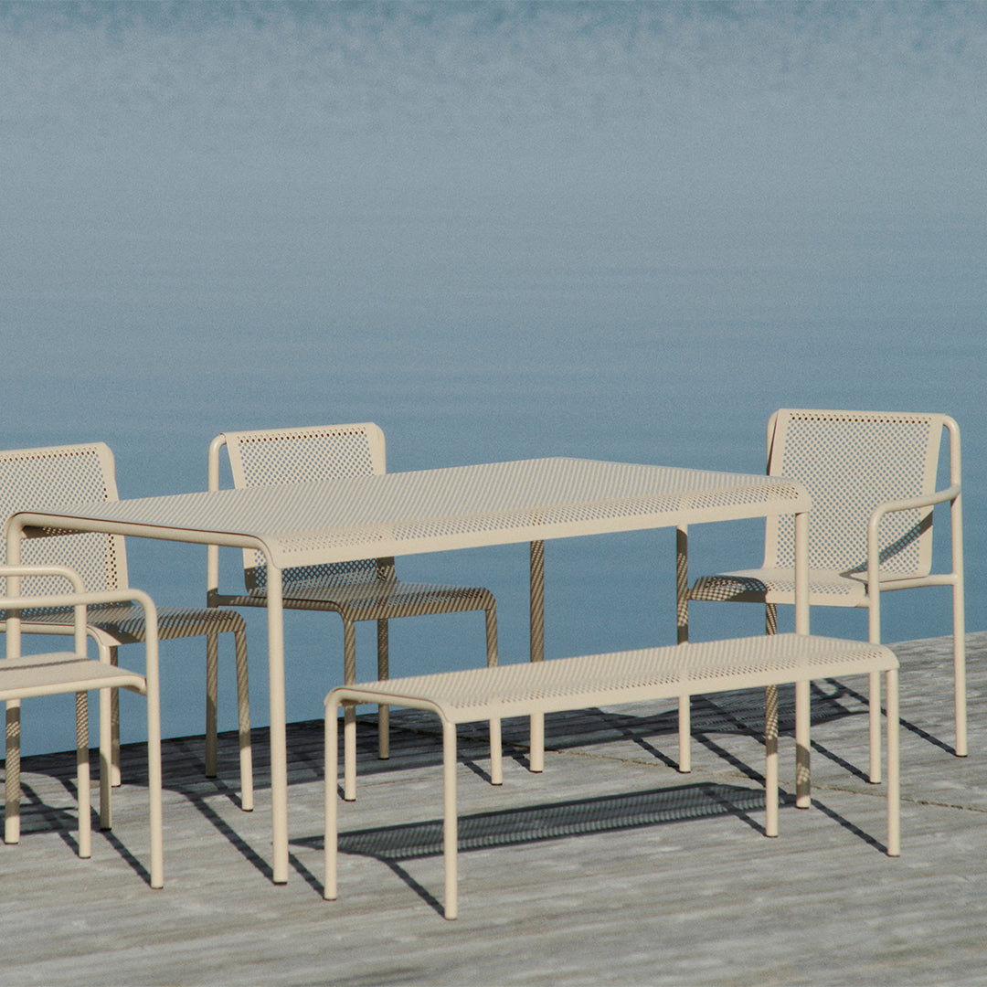 Beige outdoor dining set with perforated patterns, featuring a table and matching chairs by a serene blue water backdrop.