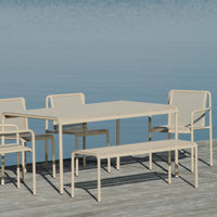 Beige outdoor dining set with perforated patterns, featuring a table and matching chairs by a serene blue water backdrop.