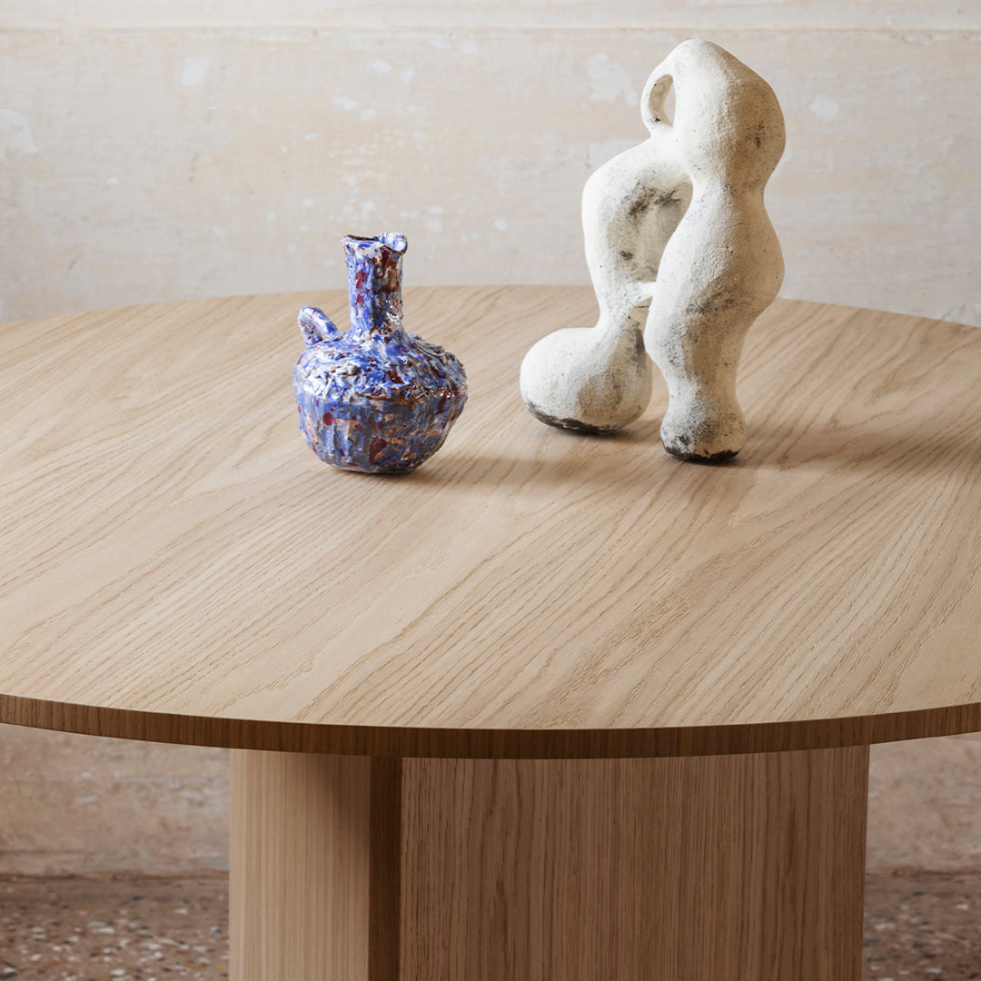 Wooden table with natural oak finish, featuring a textured blue vase and a white sculptural piece.