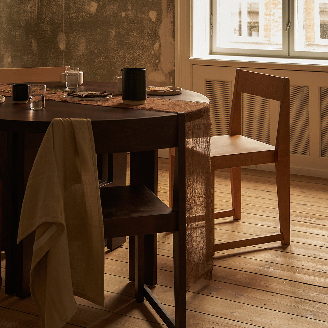Wooden dining table with natural tones, a beige linen napkin, and simple, clean-lined furniture accents.