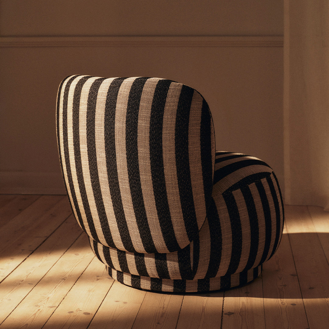 Black and beige striped lounge chair with a rounded back, set against a warm wooden floor.