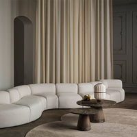 Curved white sectional sofa with soft beige curtains and minimalist decor, featuring textured round tables.