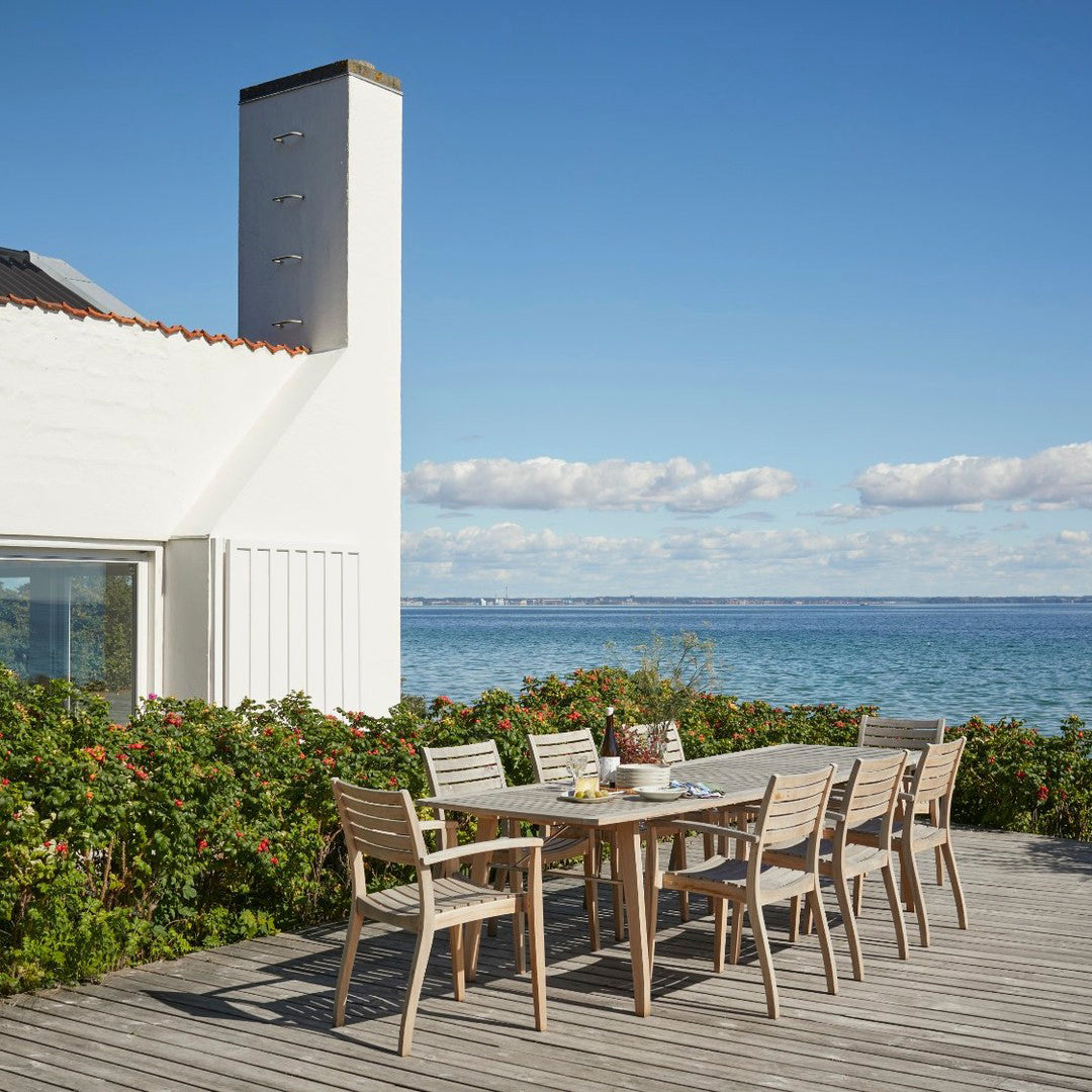 Outdoor dining set featuring natural wood tones and a minimalistic design against a vibrant coastal backdrop.