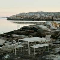 Modern white outdoor dining set against natural rocky backdrop, featuring soft earth tones and cool water reflections.
