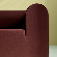 Burgundy upholstered sofa arm against a light yellow background, showcasing a smooth, textured pattern.