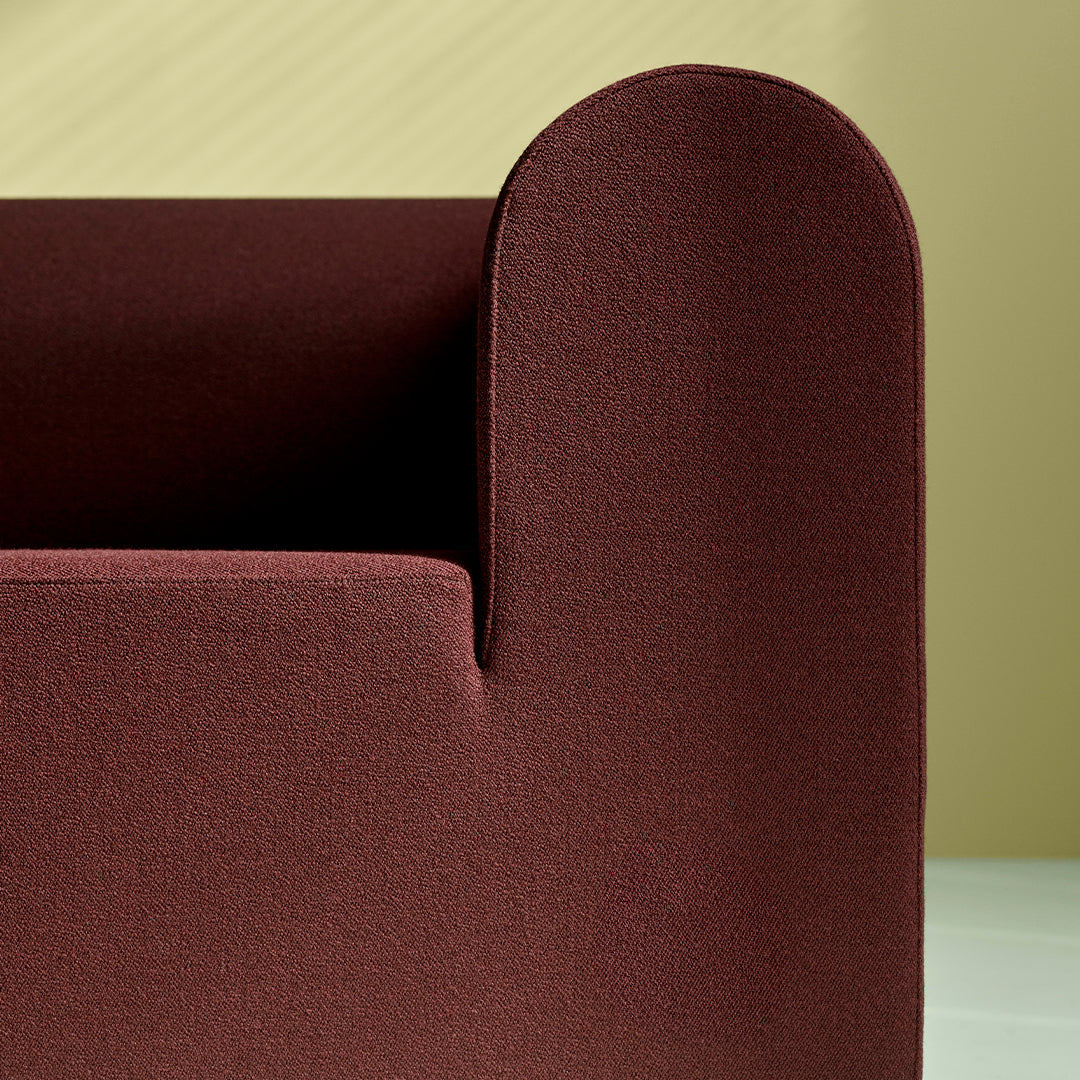 Brown textured couch with a rounded armrest against a soft yellow background. Modern, minimalist design.